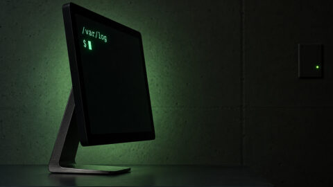 Illustration de couverture : un moniteur posé sur un bureau sombre dans une pièce technique, écran monochrome vert affichant le chemin « /var/log » puis une invite « $ » suivie d'un curseur, la lumière de l'écran éclairant un mur de béton et un voyant vert de statut au mur. Aucune personne, aucun logo.