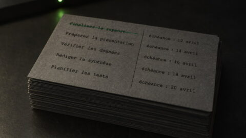 Illustration de couverture : une pile de fiches cartonnées anthracite posée sur une table graphite, un stylo graphite et un onglet vert qui dépasse de la première fiche barrée.